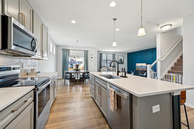 kitchen featuring light wood-style flooring, gray cabinets, a sink, appliances with stainless steel finishes, and a breakfast bar area