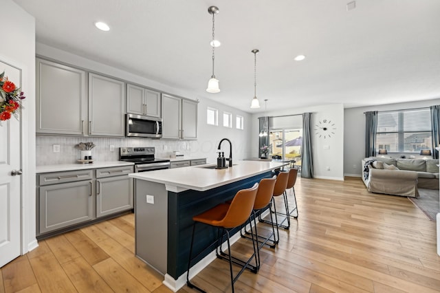 kitchen with light wood finished floors, a sink, gray cabinetry, appliances with stainless steel finishes, and backsplash