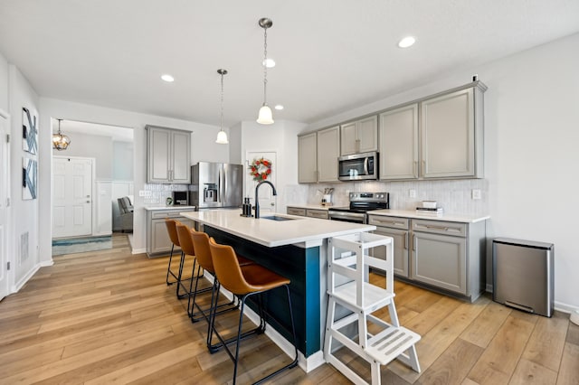 kitchen with gray cabinetry, light countertops, a kitchen breakfast bar, appliances with stainless steel finishes, and light wood-style floors