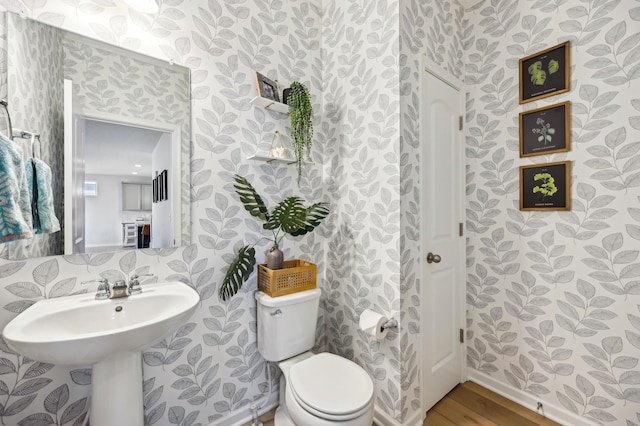 half bath with wallpapered walls, toilet, and wood finished floors