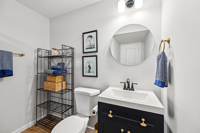 half bath with baseboards, toilet, wood finished floors, and vanity