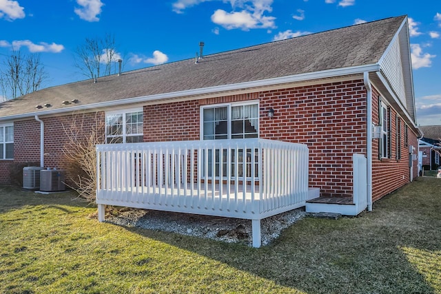 back of house featuring brick siding, central AC, roof with shingles, a lawn, and a deck