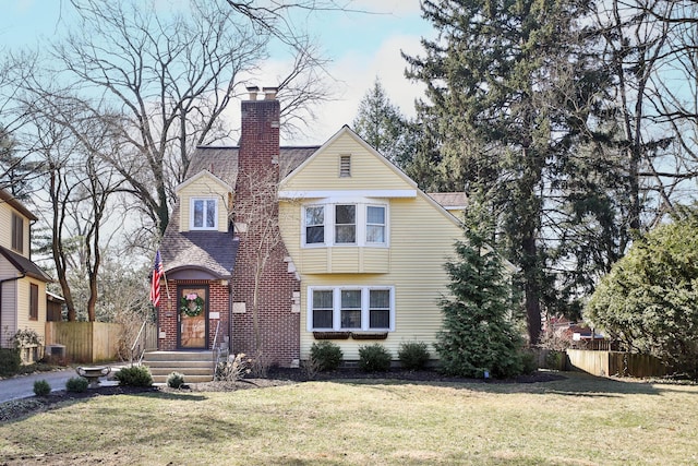 view of front of house featuring a shingled roof, a chimney, a front lawn, and fence