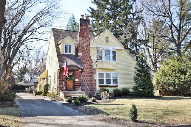 view of front of house featuring a front yard, fence, driveway, roof with shingles, and a chimney