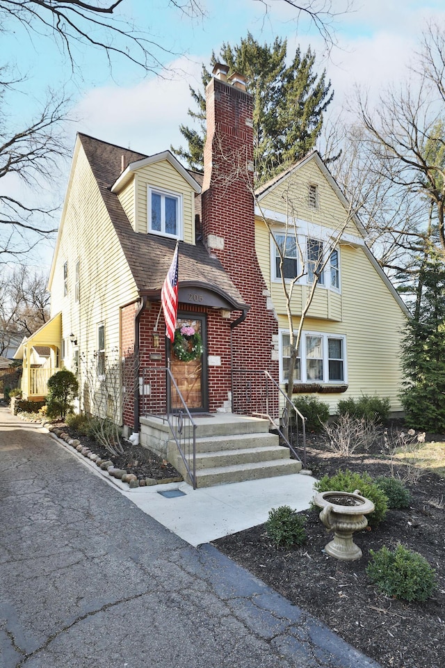 view of front of house with brick siding, roof with shingles, and a chimney