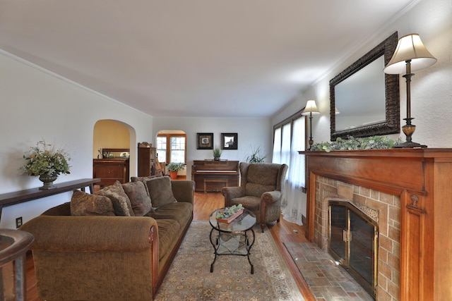 living room featuring a tiled fireplace, crown molding, plenty of natural light, and arched walkways