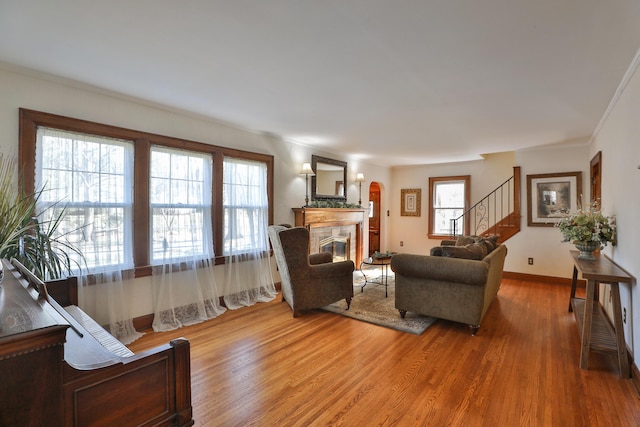 living area featuring a tiled fireplace, wood finished floors, crown molding, baseboards, and stairs