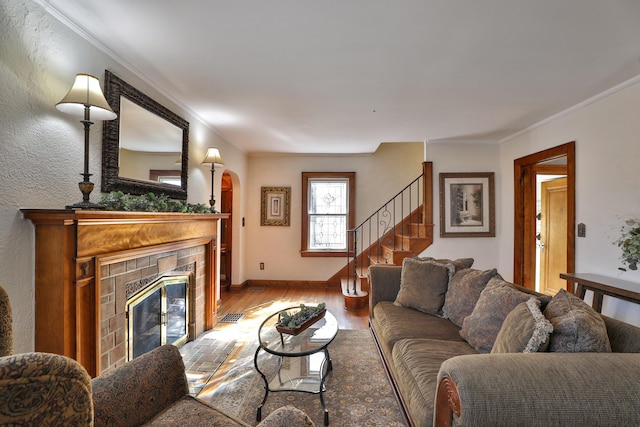 living area featuring baseboards, light wood-style floors, a tiled fireplace, and crown molding