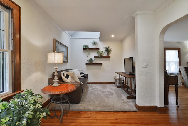 living area with baseboards, arched walkways, wood finished floors, and crown molding