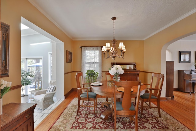 dining space with baseboards, arched walkways, ornamental molding, a notable chandelier, and light wood-type flooring