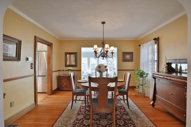 dining area featuring light wood-type flooring, a notable chandelier, ornamental molding, and a textured ceiling