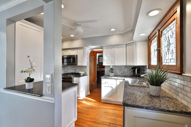 kitchen featuring stainless steel microwave, white cabinets, dark stone countertops, and light wood-style floors