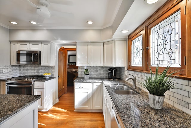 kitchen with light wood finished floors, crown molding, arched walkways, stainless steel appliances, and a sink