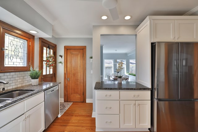 kitchen with a sink, dark stone countertops, backsplash, appliances with stainless steel finishes, and crown molding