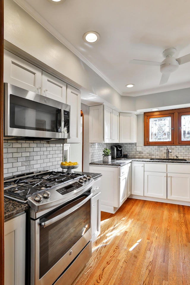 kitchen with ornamental molding, a sink, white cabinets, appliances with stainless steel finishes, and tasteful backsplash