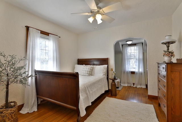 bedroom featuring wood finished floors, arched walkways, and ceiling fan