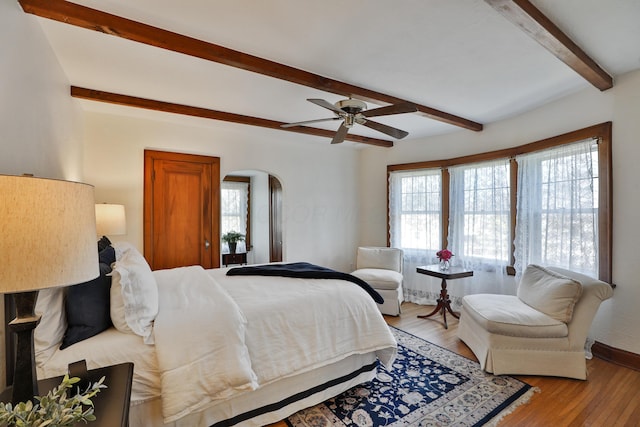 bedroom with arched walkways, beamed ceiling, multiple windows, and light wood finished floors