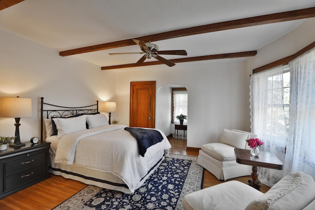 bedroom with beam ceiling, light wood-style floors, arched walkways, and ceiling fan