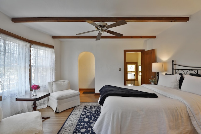 bedroom with a ceiling fan, beamed ceiling, wood finished floors, and arched walkways