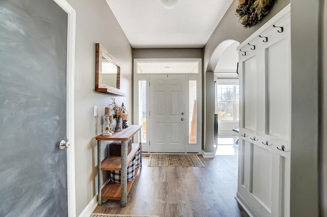 foyer entrance with wood finished floors, baseboards, and arched walkways