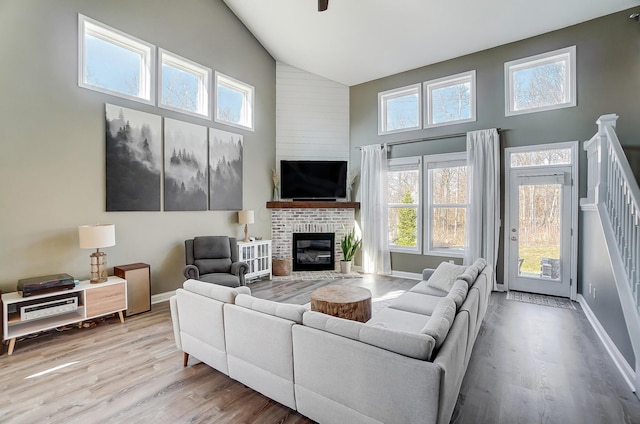 living room with a brick fireplace, baseboards, stairs, wood finished floors, and high vaulted ceiling