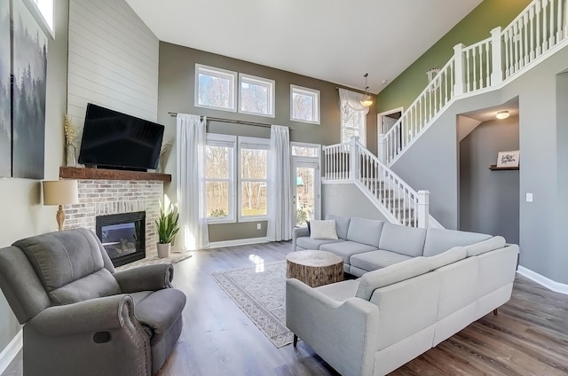 living room featuring a fireplace, a high ceiling, baseboards, and wood finished floors