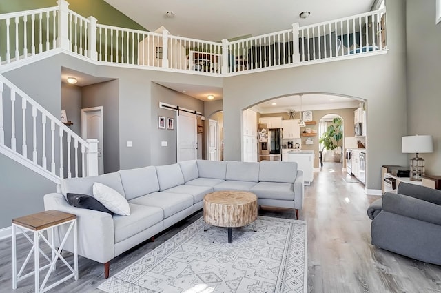 living room with baseboards, a barn door, light wood-style flooring, a high ceiling, and arched walkways