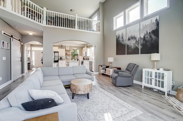 living area featuring a barn door, light wood-style flooring, baseboards, and arched walkways