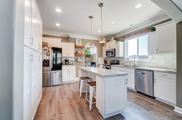 kitchen with a sink, stainless steel appliances, light wood-style floors, white cabinets, and crown molding