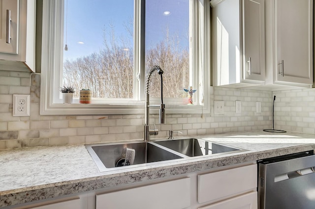 kitchen with a sink, stainless steel dishwasher, white cabinets, and light countertops