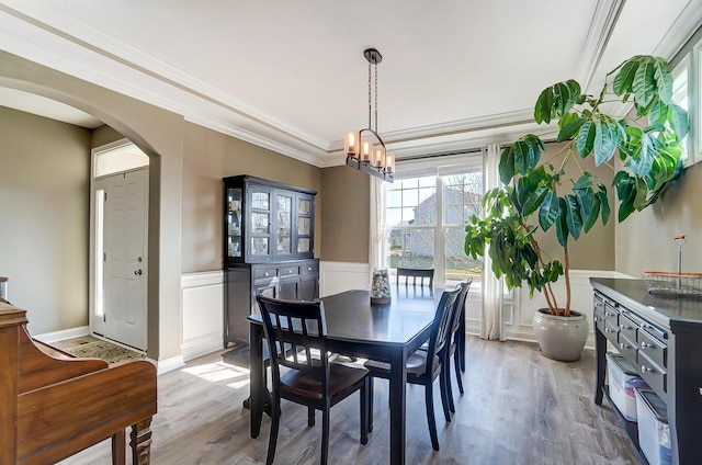 dining area with an inviting chandelier, light wood-style flooring, arched walkways, wainscoting, and crown molding