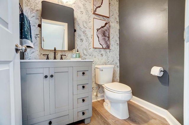 half bath featuring toilet, wood finished floors, wallpapered walls, baseboards, and vanity