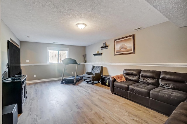 living room featuring a textured ceiling, wood finished floors, visible vents, and baseboards