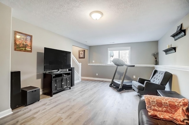 workout room featuring light wood-style floors, baseboards, and a textured ceiling