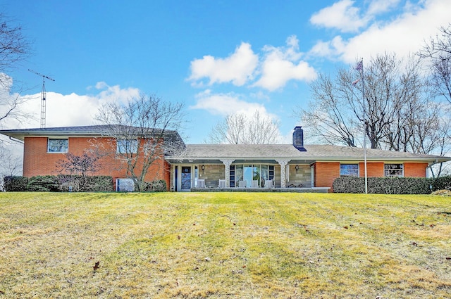 view of front of property featuring a front yard, a porch, brick siding, and a chimney