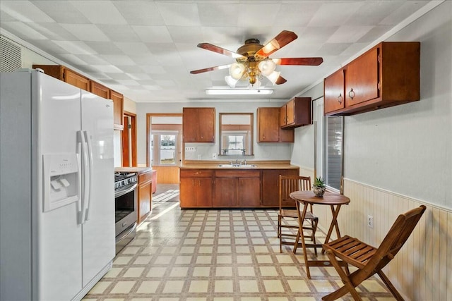 kitchen featuring a wainscoted wall, white fridge with ice dispenser, light countertops, gas range, and light floors