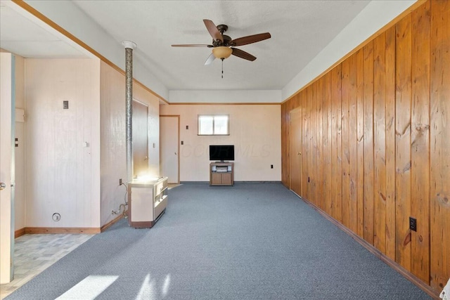 unfurnished living room featuring carpet flooring, a ceiling fan, and wood walls