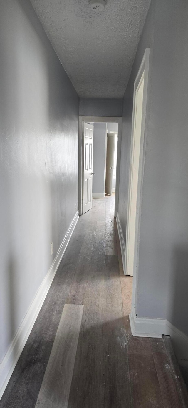 corridor featuring baseboards, a textured ceiling, and wood finished floors