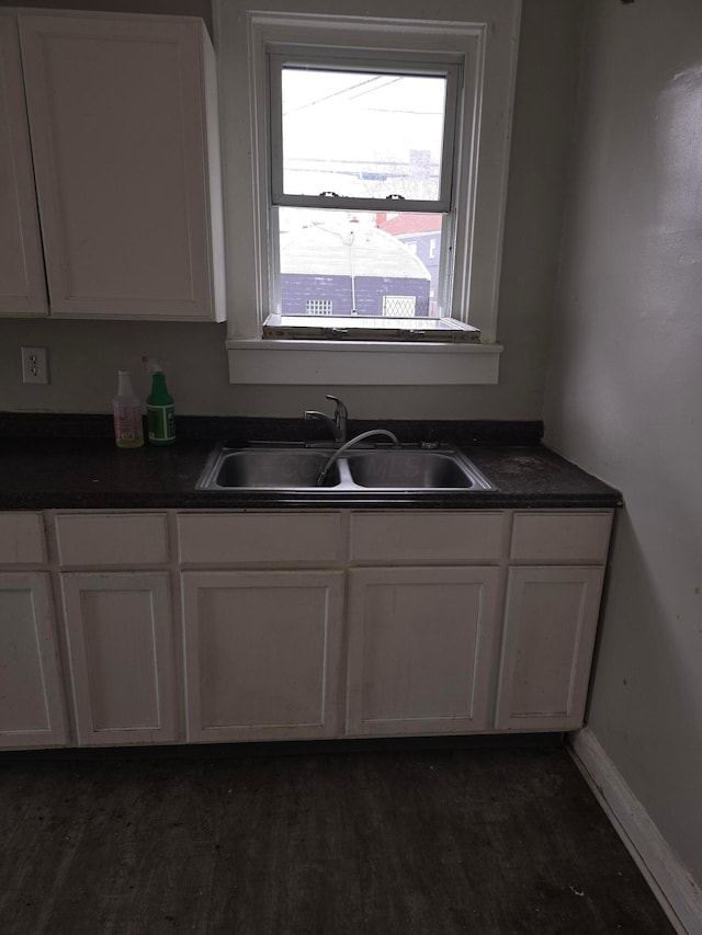 kitchen featuring baseboards, a sink, dark wood-type flooring, white cabinetry, and dark countertops