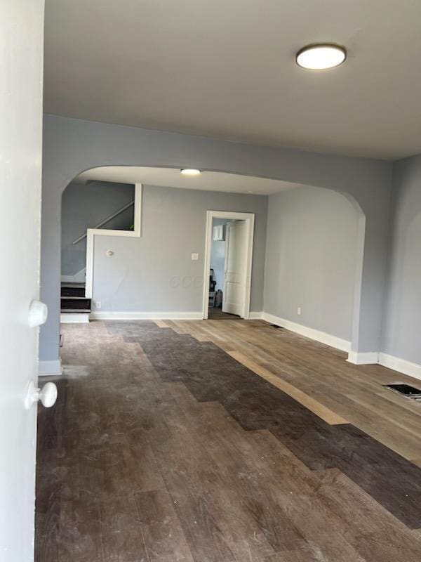 spare room with visible vents, wood finished floors, arched walkways, and baseboards