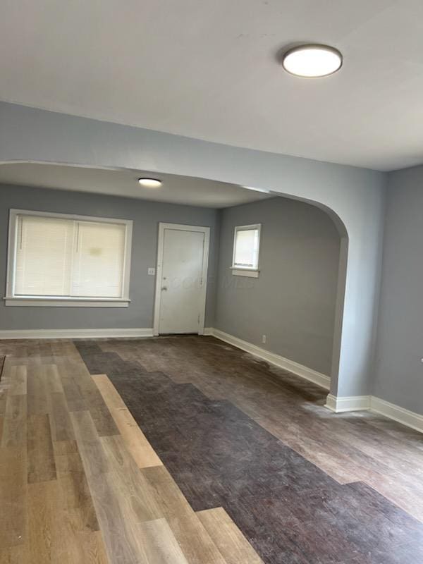 unfurnished room with arched walkways, baseboards, and wood finished floors