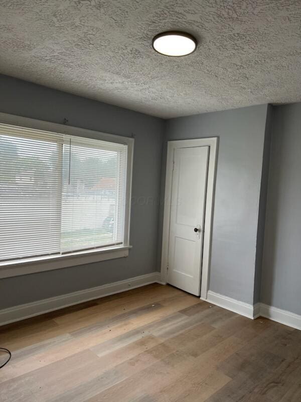 spare room with a textured ceiling, baseboards, and wood finished floors