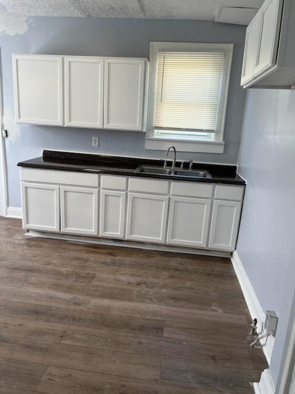 kitchen featuring white cabinetry, dark countertops, dark wood-style floors, and a sink