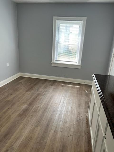 unfurnished dining area with baseboards and dark wood-style flooring