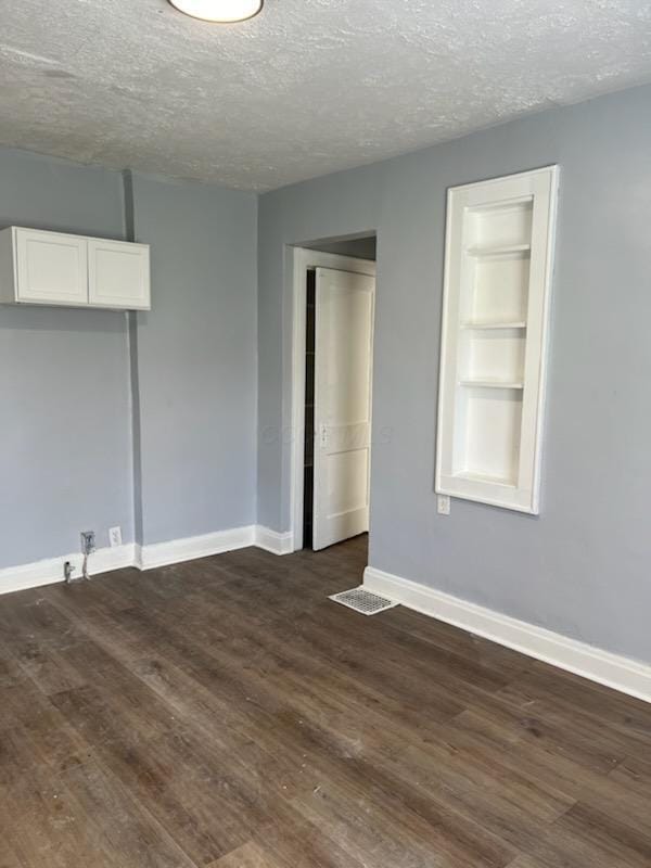 spare room with baseboards, a textured ceiling, and dark wood-style floors