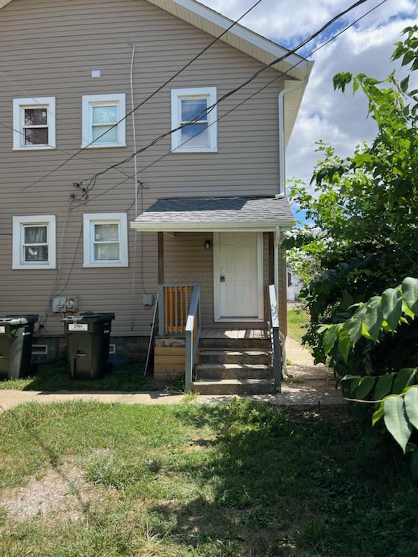 rear view of house with a lawn and roof with shingles