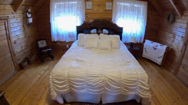 bedroom with light wood finished floors, vaulted ceiling, wood walls, and multiple windows