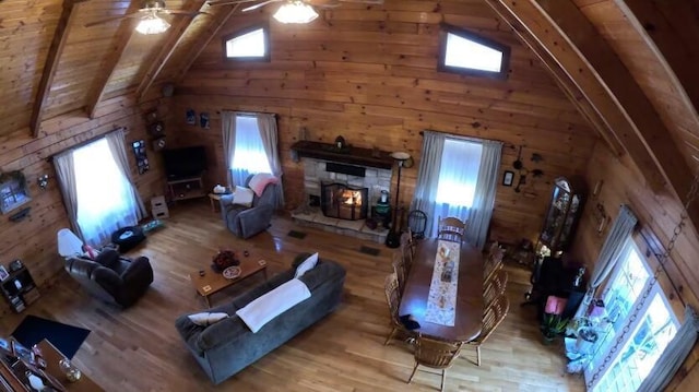 living room with a lit fireplace, wood finished floors, wood walls, and ceiling fan