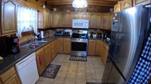 kitchen with light tile patterned floors, white appliances, dark countertops, and a sink