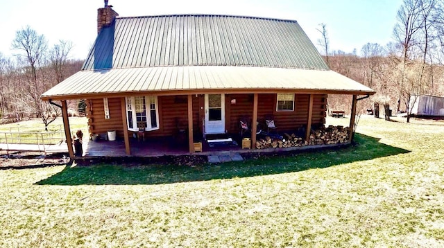 back of property featuring a lawn, metal roof, covered porch, log siding, and a chimney